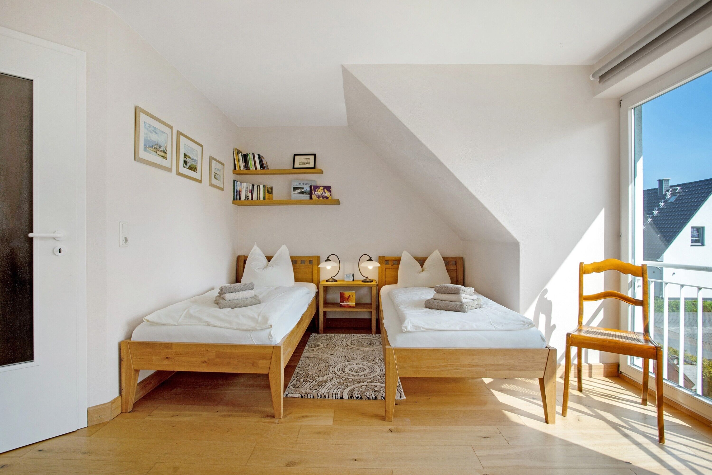 Ein Schlafzimmer mit zwei Betten, einem Holzstuhl, einem Bücherregal und einem Fenster mit Blick.