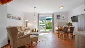 A living room with a sofa, chairs, a dining table, and a kitchen area with a TV. - Holiday Home 'Schilfblick' with Lake View, Private Terrace and Wi-Fi (Wieck a Darß)