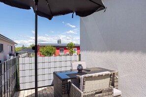 Ein Balkon mit Tisch und Stühlen, einem Metallzaun und einem Gebäude im Hintergrund.