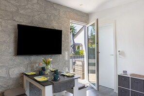 Ein modernes Interieur mit einer Steinwand, einem Flachbildfernseher, einem Esstisch mit Tellern und Gläsern sowie einer Schiebeglastür, die zu einem Außenbereich führt.