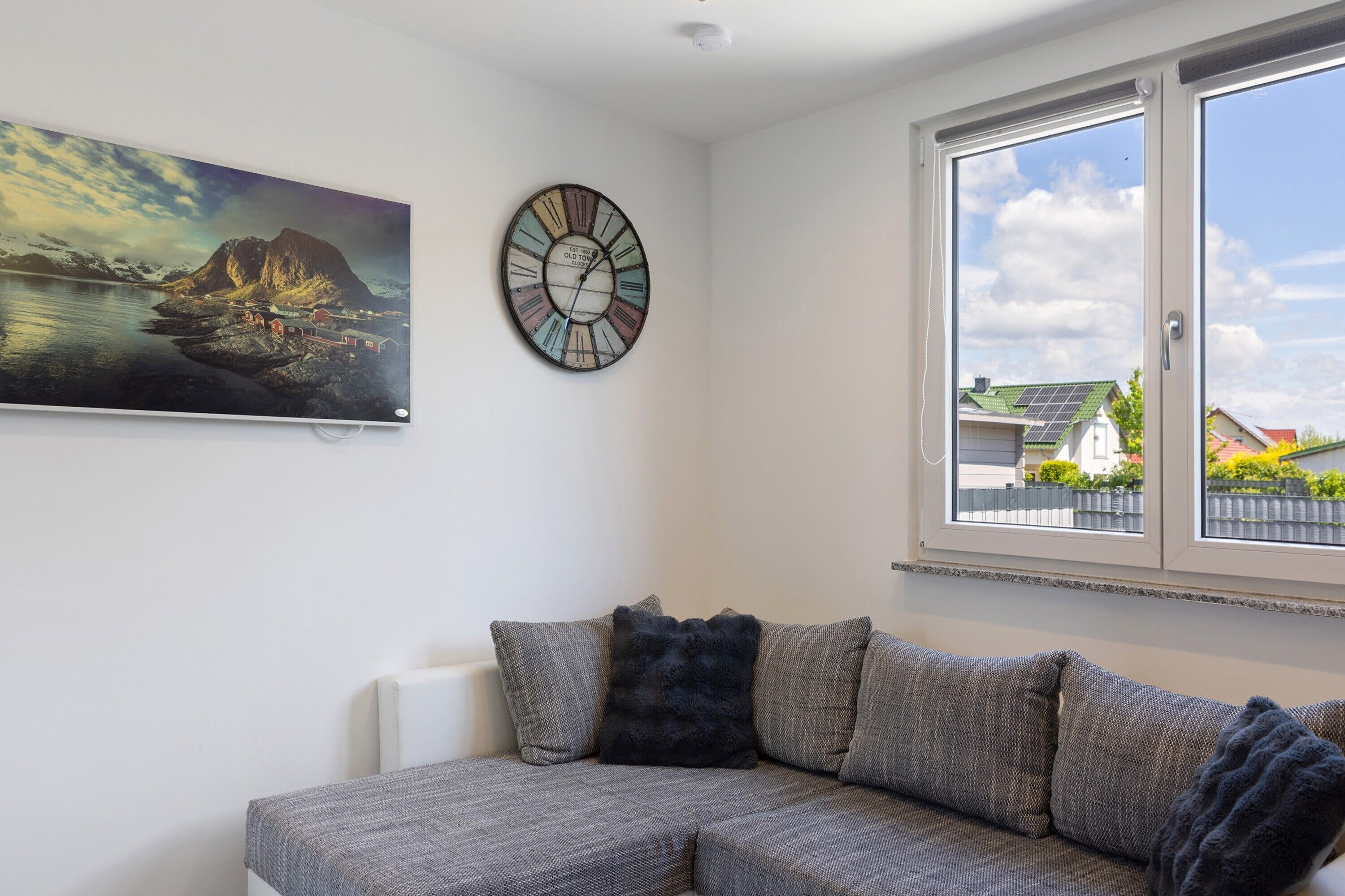 Ein Wohnzimmer mit einer Couch, einer Wanduhr, einem Gemälde und einem Fenster mit Blick.