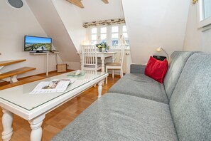 Tunnelmallinen olohuone, jossa on harmaa sohva, valkoinen sohvapöytä ja televisio, josta näkyy kaunis maisema.