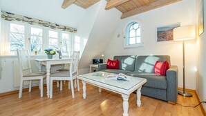 Un espacio habitable estilo loft acogedor, con comedor, sofá gris y cojines rojos, y un ventanal que proporciona luz natural.