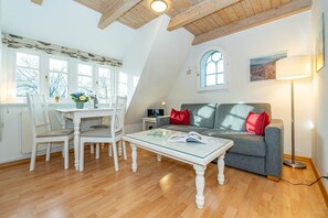 Un espace de vie chaleureux de style loft, comprenant un coin repas, un canapé gris agrémenté de coussins rouges et une grande fenêtre laissant entrer la lumière naturelle.