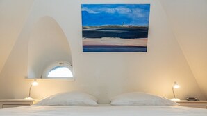 Un dormitorio con cama, dos lámparas de noche, una ventana y un cuadro de una playa.