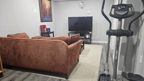 Un salon avec un canapé marron, un téléviseur, un tapis de course et une horloge au mur.