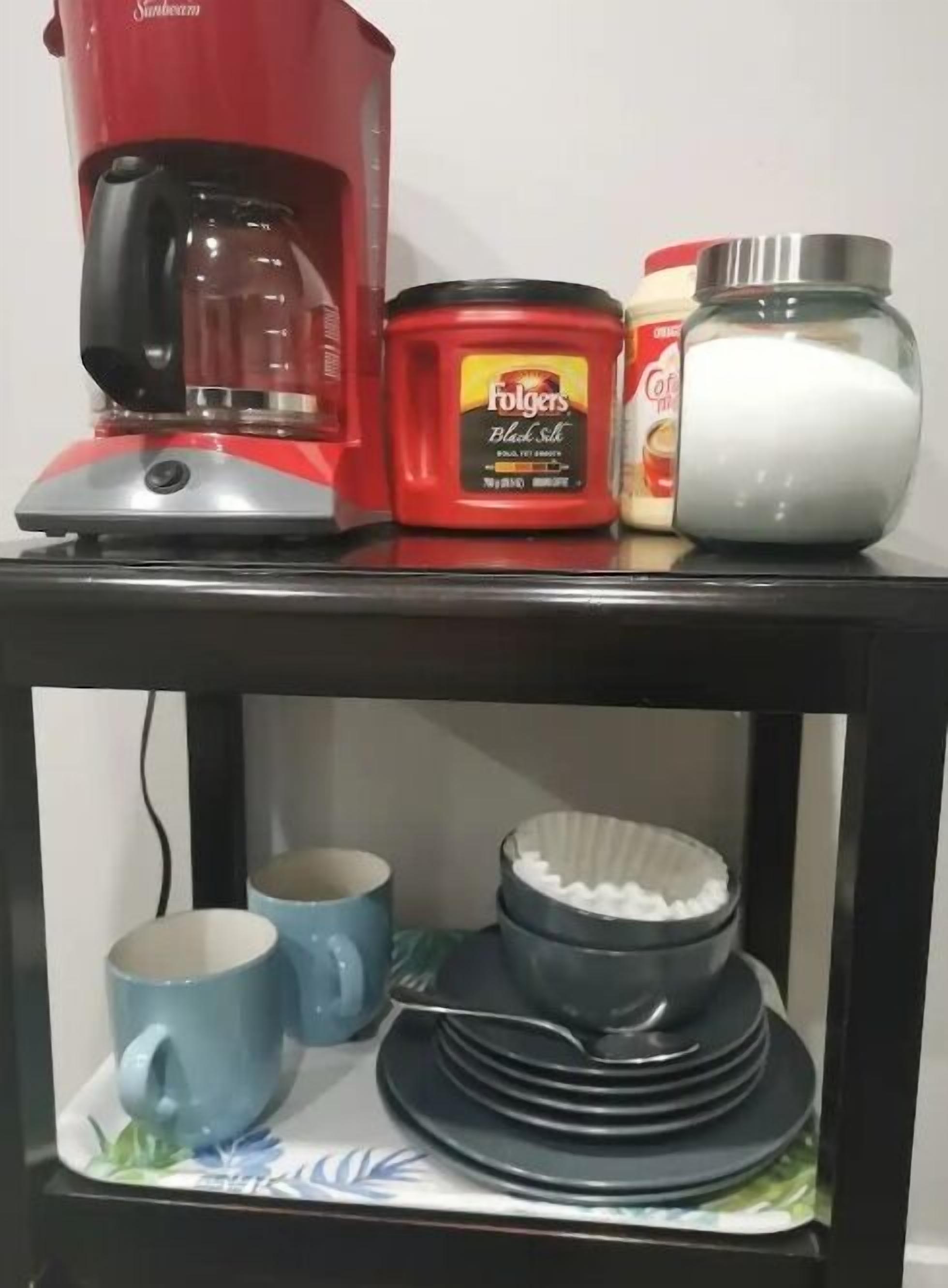 Eine Küchenarbeitsplatte mit einer roten Kaffeemaschine, einem Glas Folgers Black & White Kaffee, einer Milchpackung und einem Stapel Teller und Schüsseln.