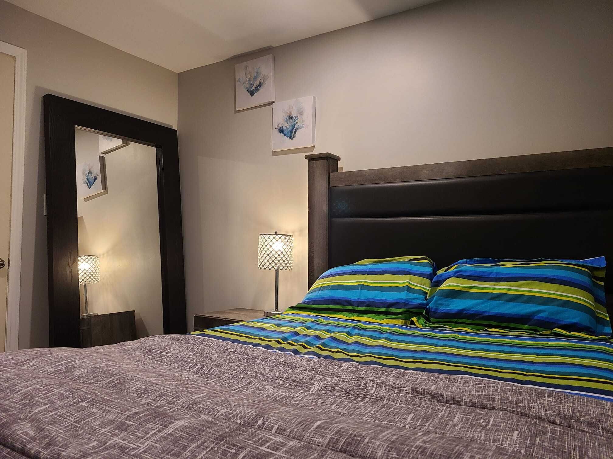 Une chambre à coucher avec un lit, une table de chevet, une lampe et des œuvres d’art murales.