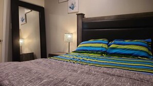 Une chambre à coucher avec un lit, une table de chevet, une lampe et des œuvres d’art murales.