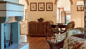 Un comedor con mobiliario de mimbre, un armario de madera e impresiones botánicas enmarcadas en la pared.