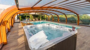 A hot tub with a wooden canopy and a poolside area with lounge chairs and a view of greenery.
