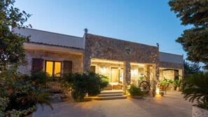 A stone building with a courtyard, featuring a well-lit entrance and surrounding greenery.