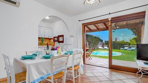 A dining area with a table set for four, a kitchen in the background, and a pool area visible through a glass door.