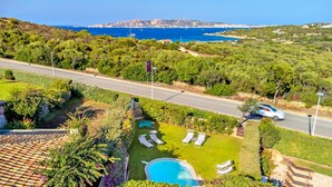 A pool area with lounge chairs, a swimming pool, and a view of the sea.