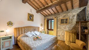 Ein Schlafzimmer mit einem großen Bett, Holzbalken, Steinwänden und einem kleinen Tisch mit Stuhl.