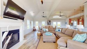 A spacious living room with a fireplace, a large sectional sofa, and a television mounted above it. - Sundancer - 5 bedrooms with elevator! (Bald Head Island)