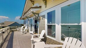 Eine überdachte Terrasse mit weißen Stühlen und einer Glastür, die zu einem Gebäude führt.