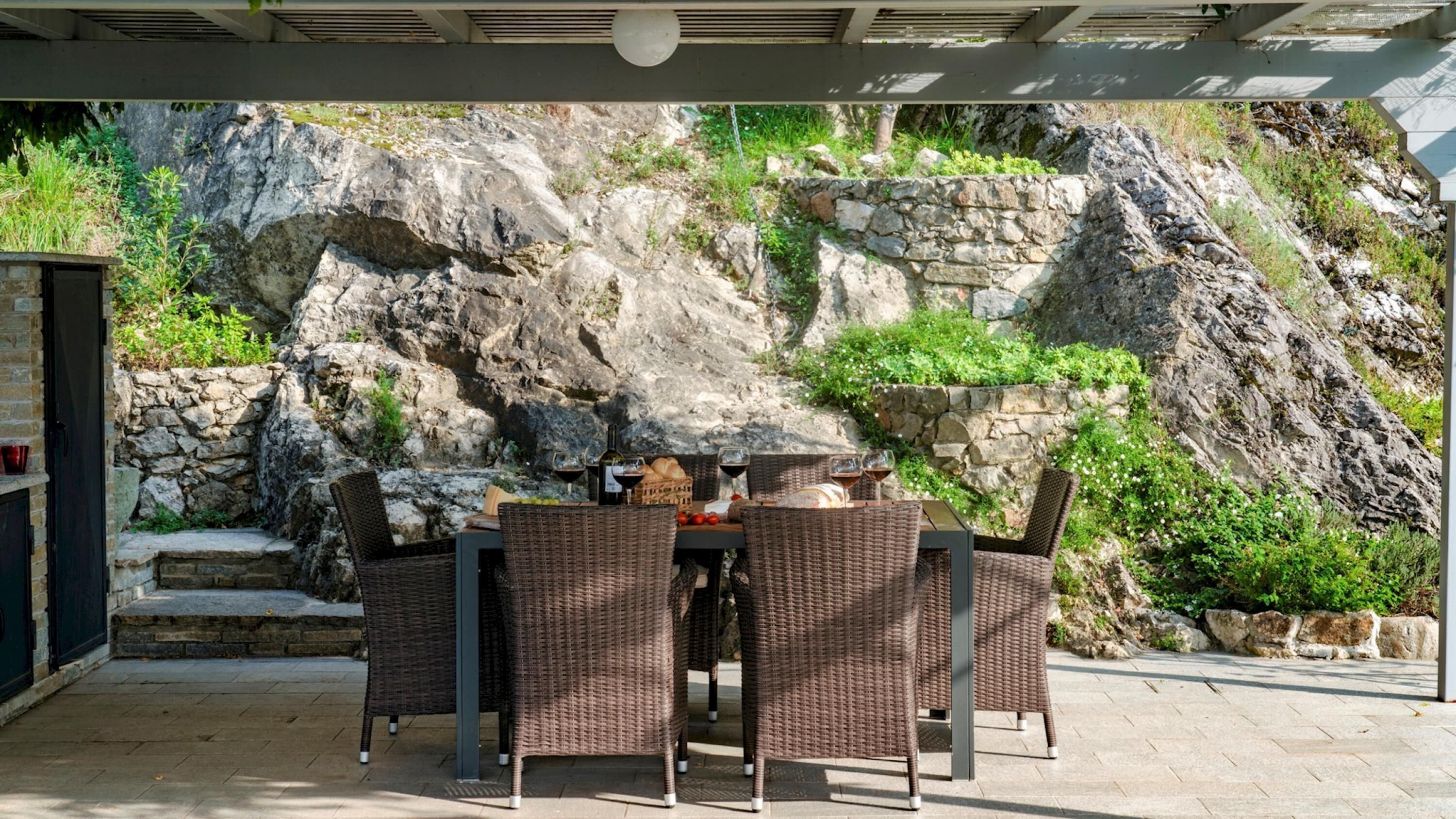An outdoor patio with wicker furniture, a stone wall, and a rocky backdrop.