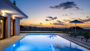 A modern pool area with a sunset view, outdoor seating, and a stone wall.
