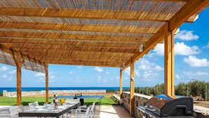 An outdoor dining area with a view of the sea, a grill, and a table set for two.