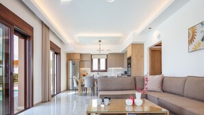 A modern living room with a glass coffee table, a sofa, and a dining area with chairs.