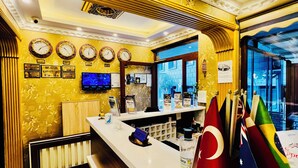 A hotel reception area with a white reception desk, multiple clocks on the wall, and flags of various countries.