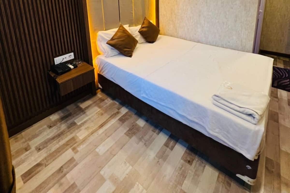 Habitación de hotel moderna con una cama grande, paneles de madera y una mesita de noche con teléfono y cargador.