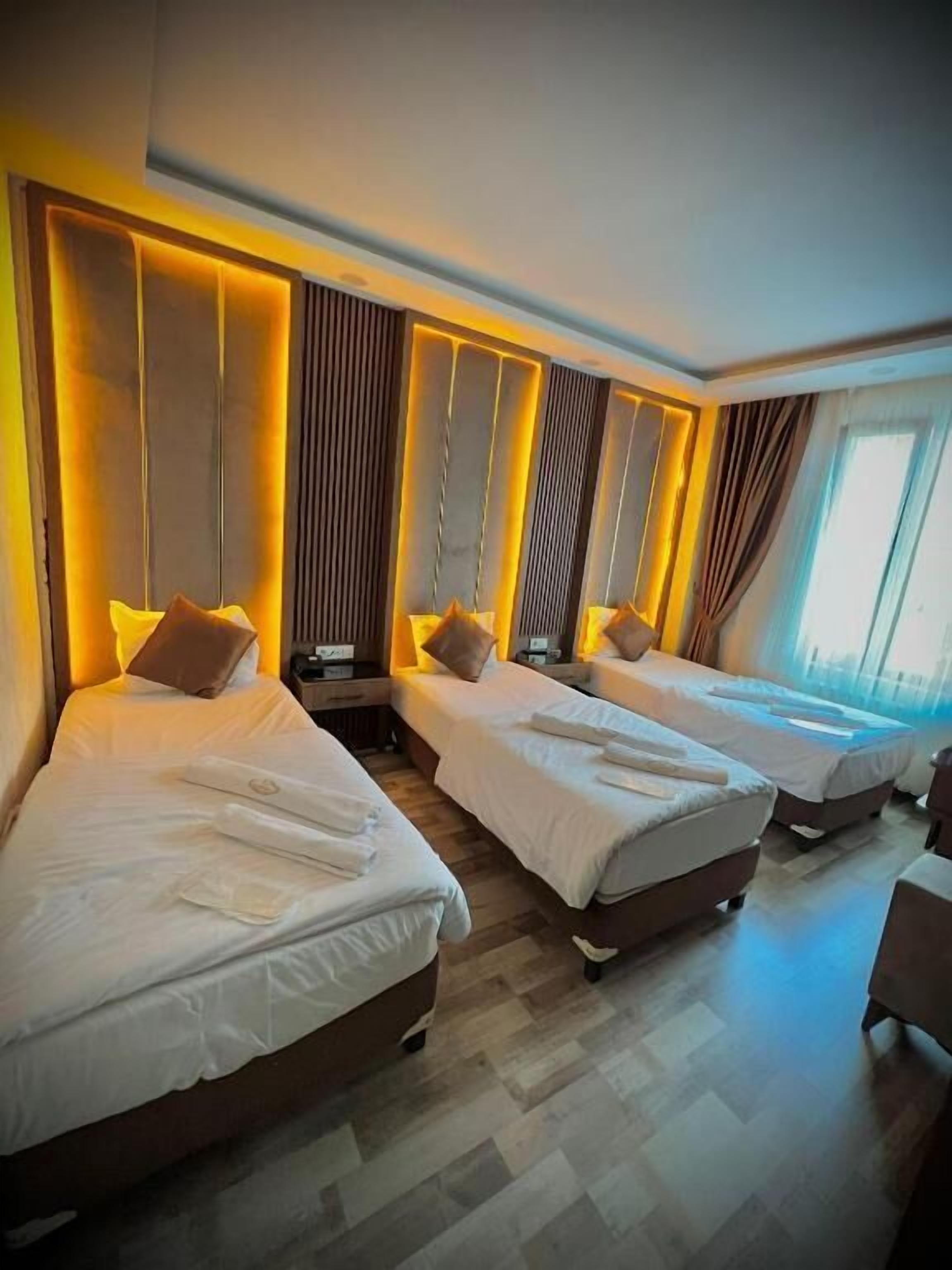 A hotel room with three beds arranged in a row, each with white linens and pillows. The room features a modern design with wooden paneling on the walls and a wooden floor.