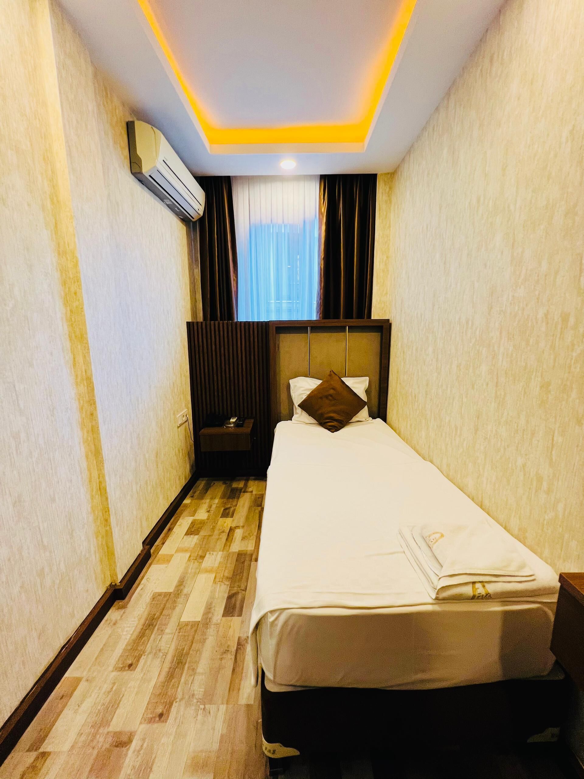 A hotel room with a bed, a nightstand, a window with curtains, and a ceiling with recessed lighting.