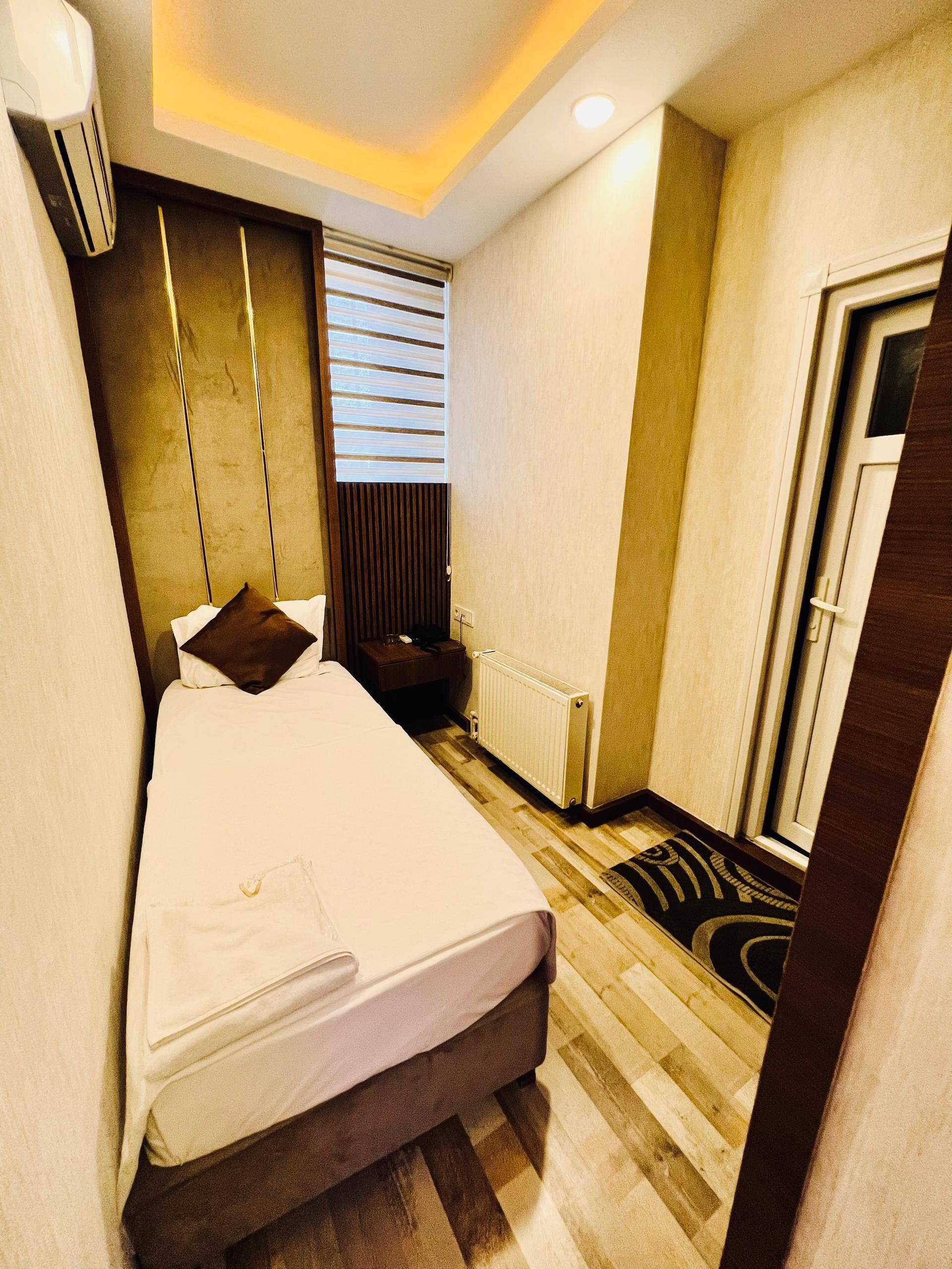 A hotel room with a bed, a radiator, a window with blinds, and a door.