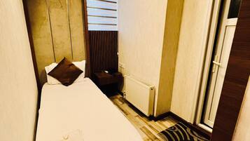 A hotel room with a bed, a radiator, a window with blinds, and a door.