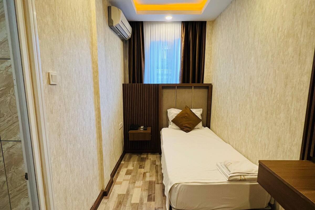 Una habitación de hotel compacta con cama, mesita de noche y pequeño atril.