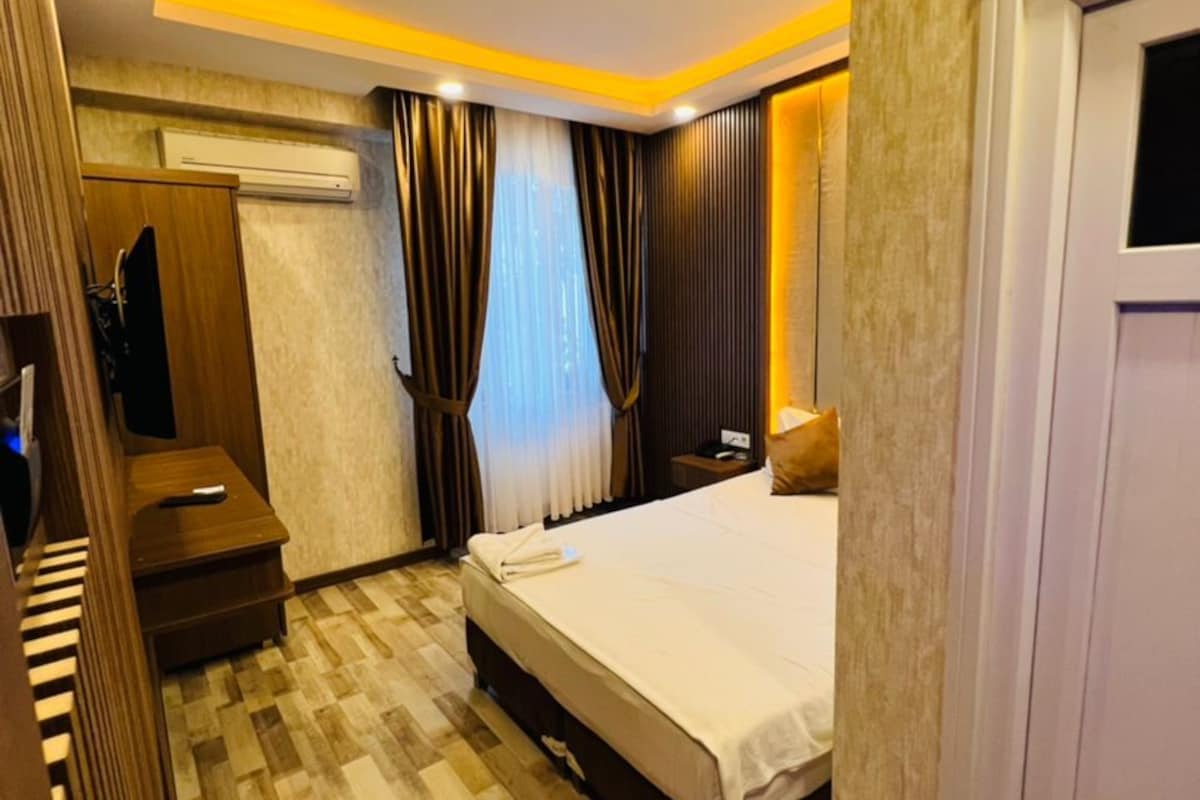 A hotel room with a bed, a desk, a wardrobe, and an air conditioning unit.