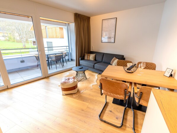 Ein modernes Wohnzimmer mit Sofa, Esstisch und einer großen Schiebeglastür, die zu einem Außenbereich führt.