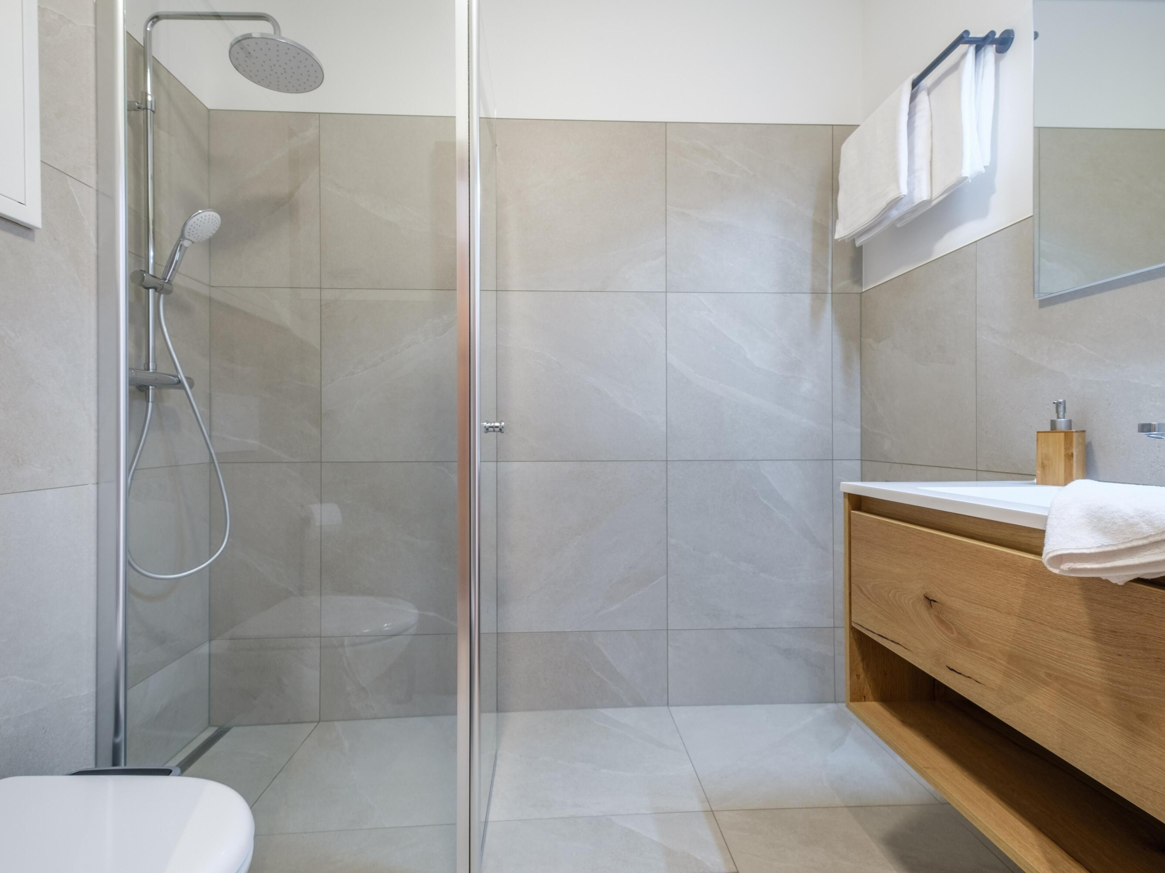 Ein modernes Badezimmer mit einer gläsernen Dusche, einem Holzauszug und einer weißen Toilette.