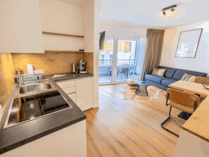 Cocina moderna con estufa integrada, cafetera y lavamanos. Cuenta con comedor con mesa y sillas, y una sala de estar con sofá y mesa de centro.