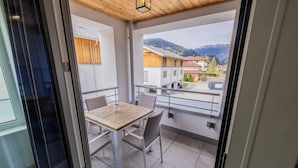 Un balcón con mesa y sillas, vista a edificios y montañas, y techo de madera.