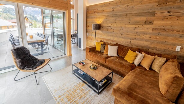 Una sala de estar moderna con una pared de madera, un sofá marrón y un ventanal que da a un espacio exterior.