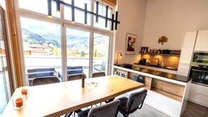 Una cocina moderna con una mesa y sillas de madera, ventanas amplias con vistas a la montaña y un horno empotrado.