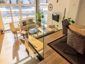 Relax in a spacious living area with a sofa, chairs, and dining table, offering a clear view of the outdoors through large windows.