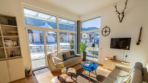 Una sala de estar moderna con sofá, mesa de centro y estantería. Amplias ventanas ofrecen vistas a un paisaje nevado.
