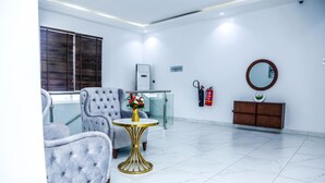 A hotel lobby with a seating area, a small table with a vase, a fire extinguisher, a mirror, and a cabinet. - Stratton 38 Asokoro (Abuja)