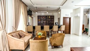 A living room with a sofa, armchairs, a coffee table, and a bar area with shelves of bottles. - Stratton 38 Asokoro (Abuja)