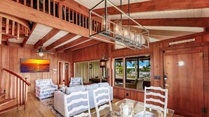 A wooden interior with a glass dining table, striped sofa, and a staircase.