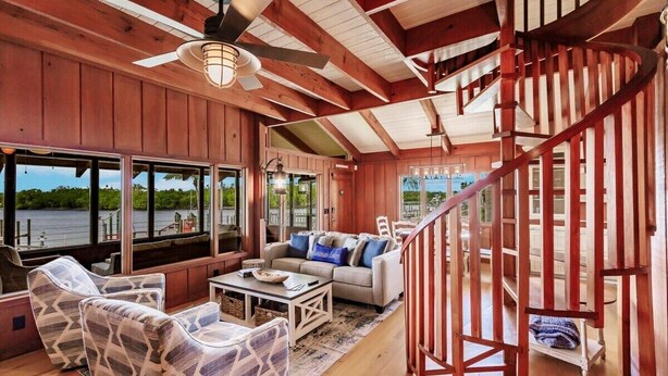 A spacious cabin interior with a wooden interior, a sofa, chairs, a dining table, and a staircase.
