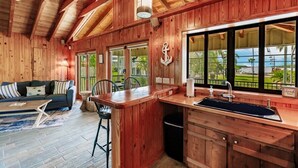 A wooden interior with a kitchen area, a sofa, and a view of the outdoors.