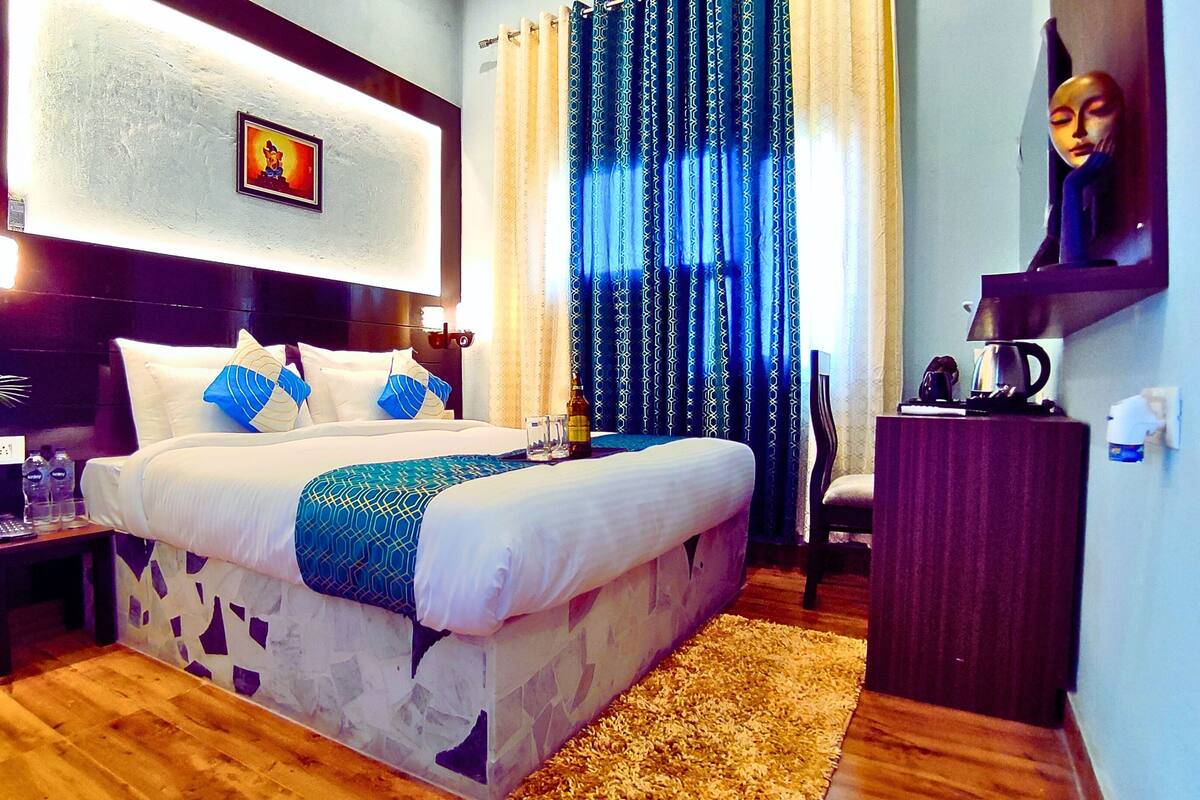 Ein Hotelzimmer mit Bett, Nachttisch, Schreibtisch, Stuhl, Blumentopf und einem Bild an der Wand.