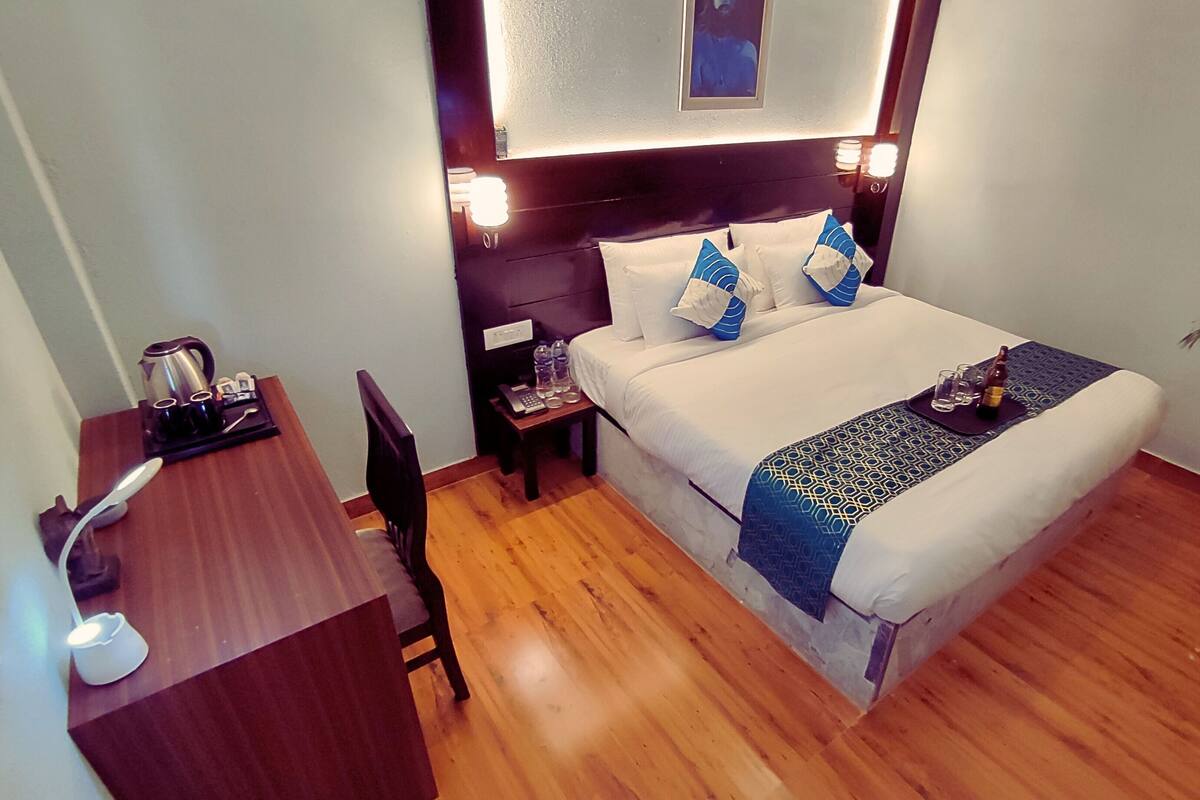 Ein Hotelzimmer mit Bett, Nachttisch, Stuhl und Schreibtisch, inklusive Wasserkocher und Tassen.