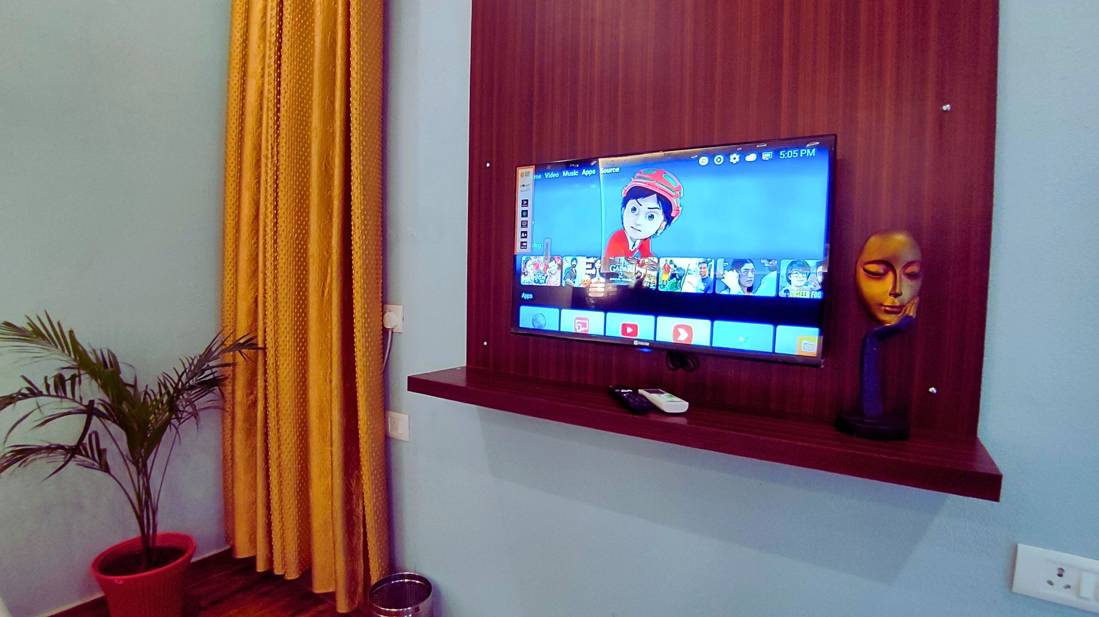 Un televisor montado en una pared de madera con un estante debajo donde se exhibe un control remoto.