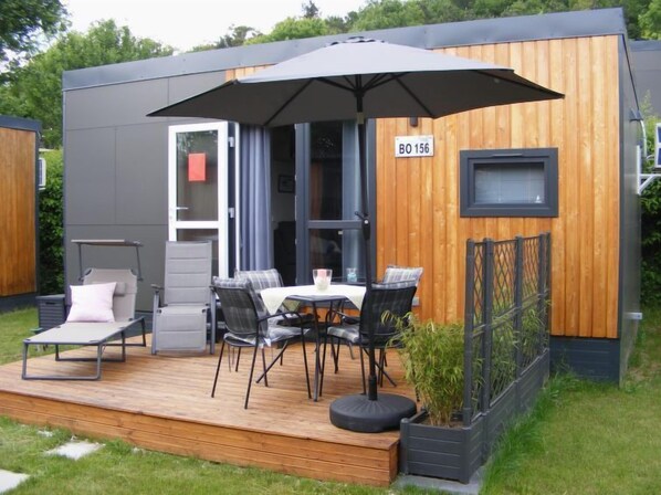A modern outdoor patio area with a table and chairs, a lounge chair, and a large umbrella.